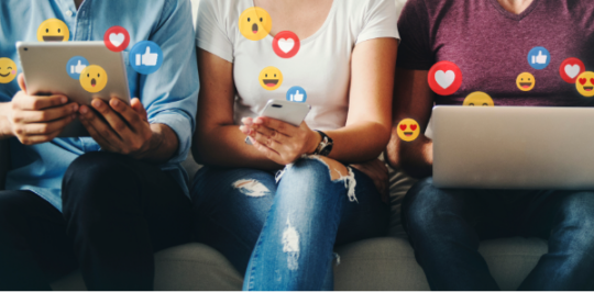 Three people using electronic devices, surrounded by emoji reactions representing engagement on social media.